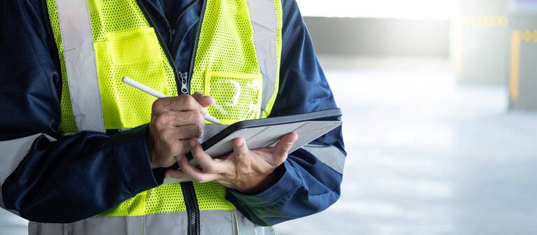 Bauinspektor mit digitalem Tablet, Überprüfung der Sicherheit und Sicherheitssystem im Gebäude. Männlicher Arbeiter in reflektierender Weste, der für die Gebäudeinspektion arbeitet