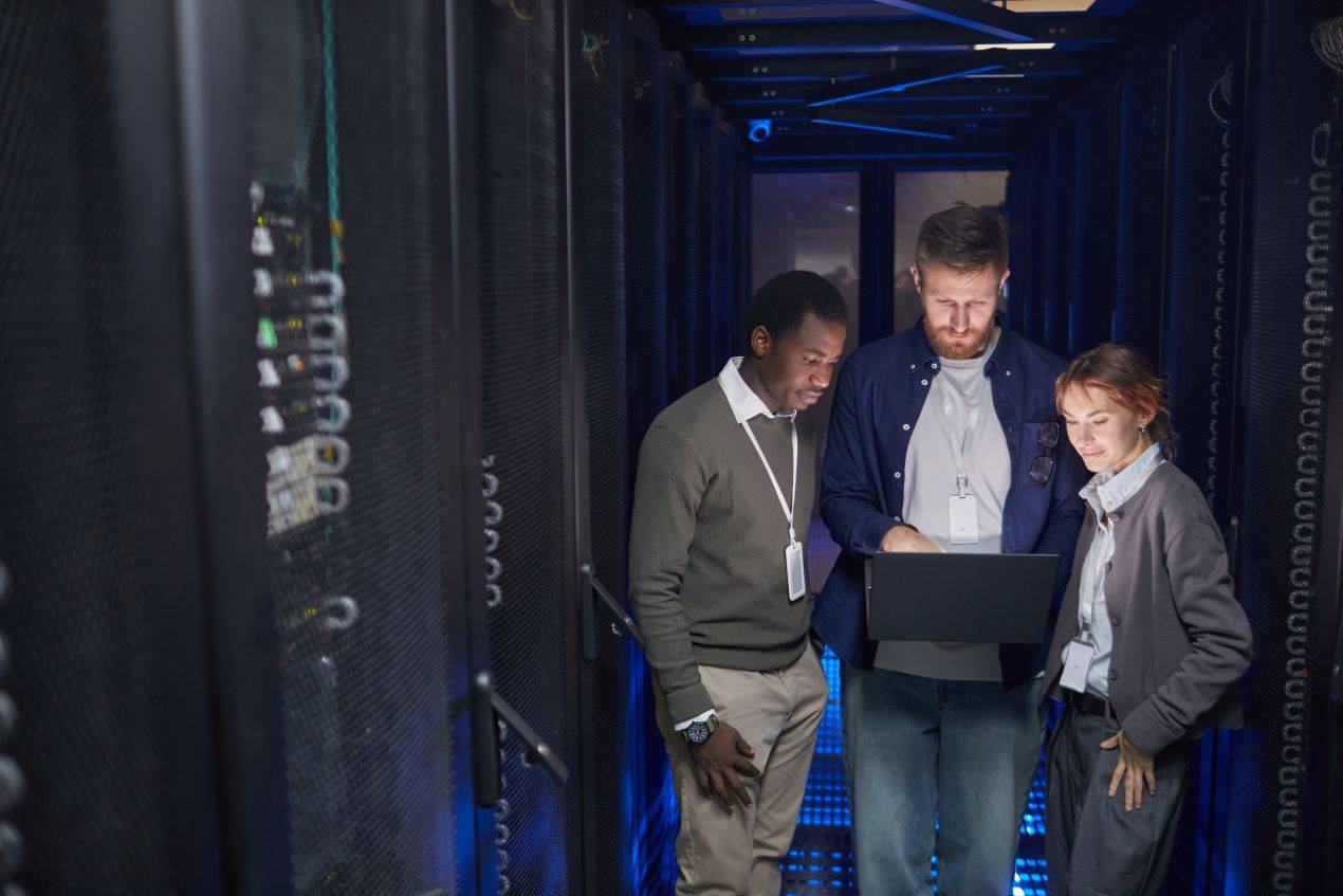 Drei Personen im Serverraum sehen auf Laptop – Zusammenarbeit bei E-Learning Datenschutz