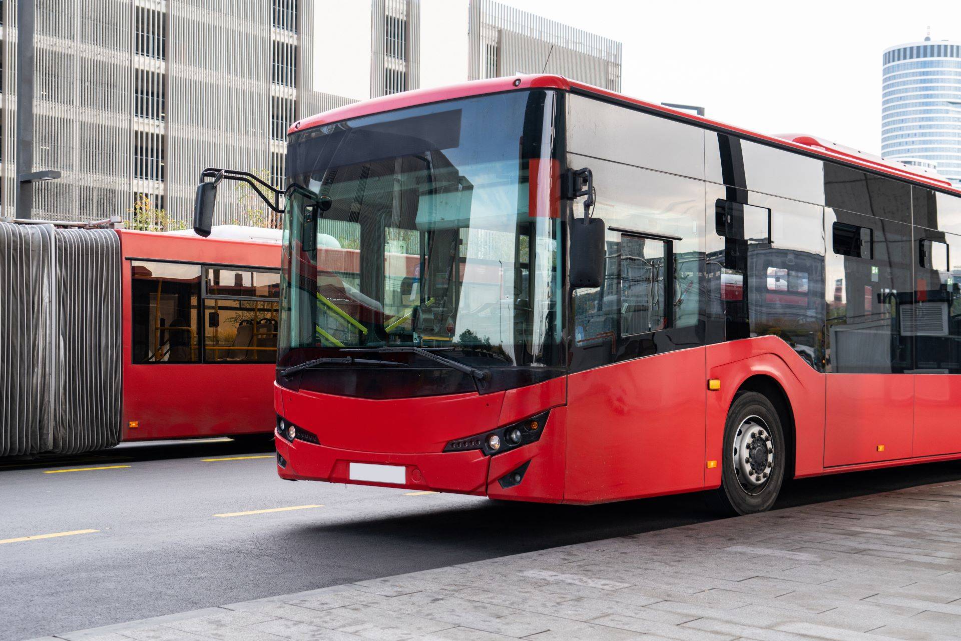 Moderner roter Stadtbus im Stadtverkehr mit Hochhäusern im Hintergrund, Symbol für Stellenangebote ÖPNV